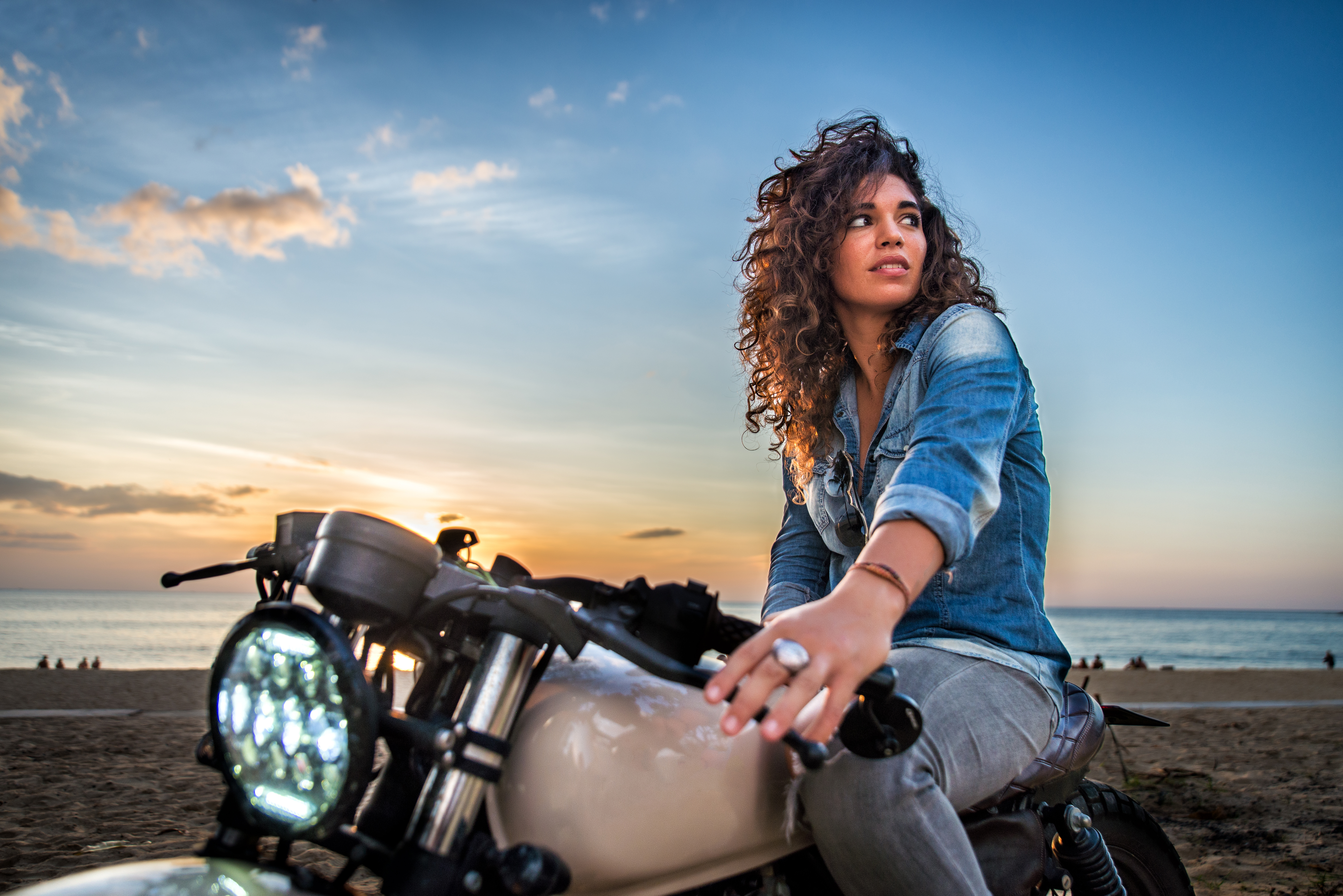 Mujer en café racer junto al mar al atardecer